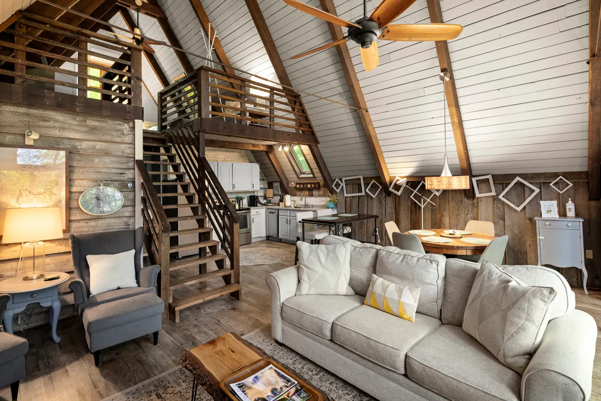 An open-plan living area where a cozy sofa, a dining table with chairs, a visible kitchen, and a wooden staircase are all seamlessly integrated. The atmosphere is warm and welcoming, perfect for movie nights, dinner parties, or quiet evenings in.