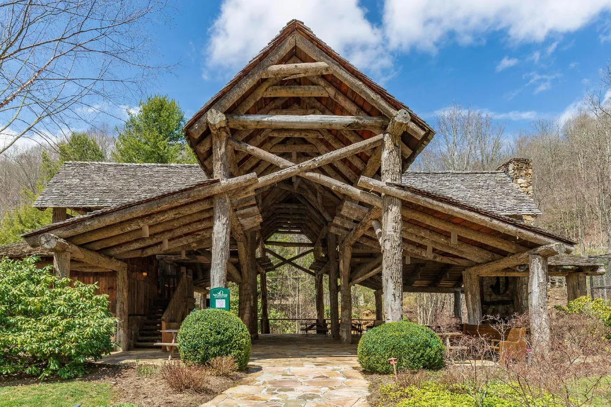 A rustic wooden structure with open space beneath its roof sits beside a stone pathway surrounded by lush green foliage. The setting is cozy yet expansive, ideal for enjoying coffee with sunrise, relaxing afternoons, or stargazing in the evening.