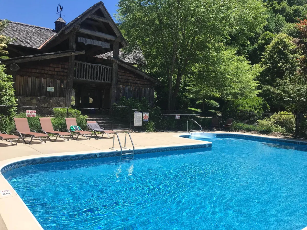 This image features the community swimming pool, complete with lounge chairs and a rustic wooden lodge in the background. Families and groups are depicted enjoying the poolside atmosphere, suggesting both relaxation and lively activity. The scene is bathed in natural sunlight, creating a welcoming and leisurely environment.