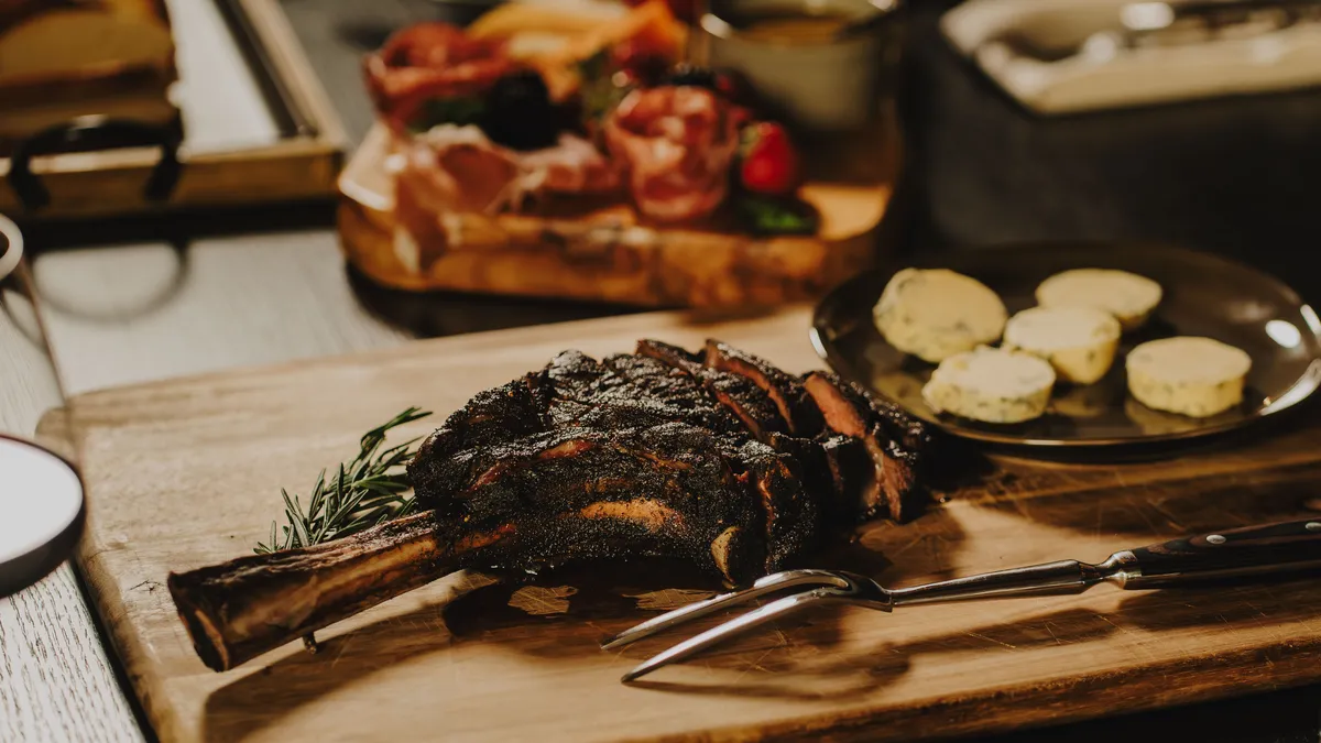 A beautifully set dining table with a rib roast, flavored butter, and an assortment of charcuterie, radiating warmth and conviviality. The setting emphasizes gourmet cuisine and the pleasure of shared meals.