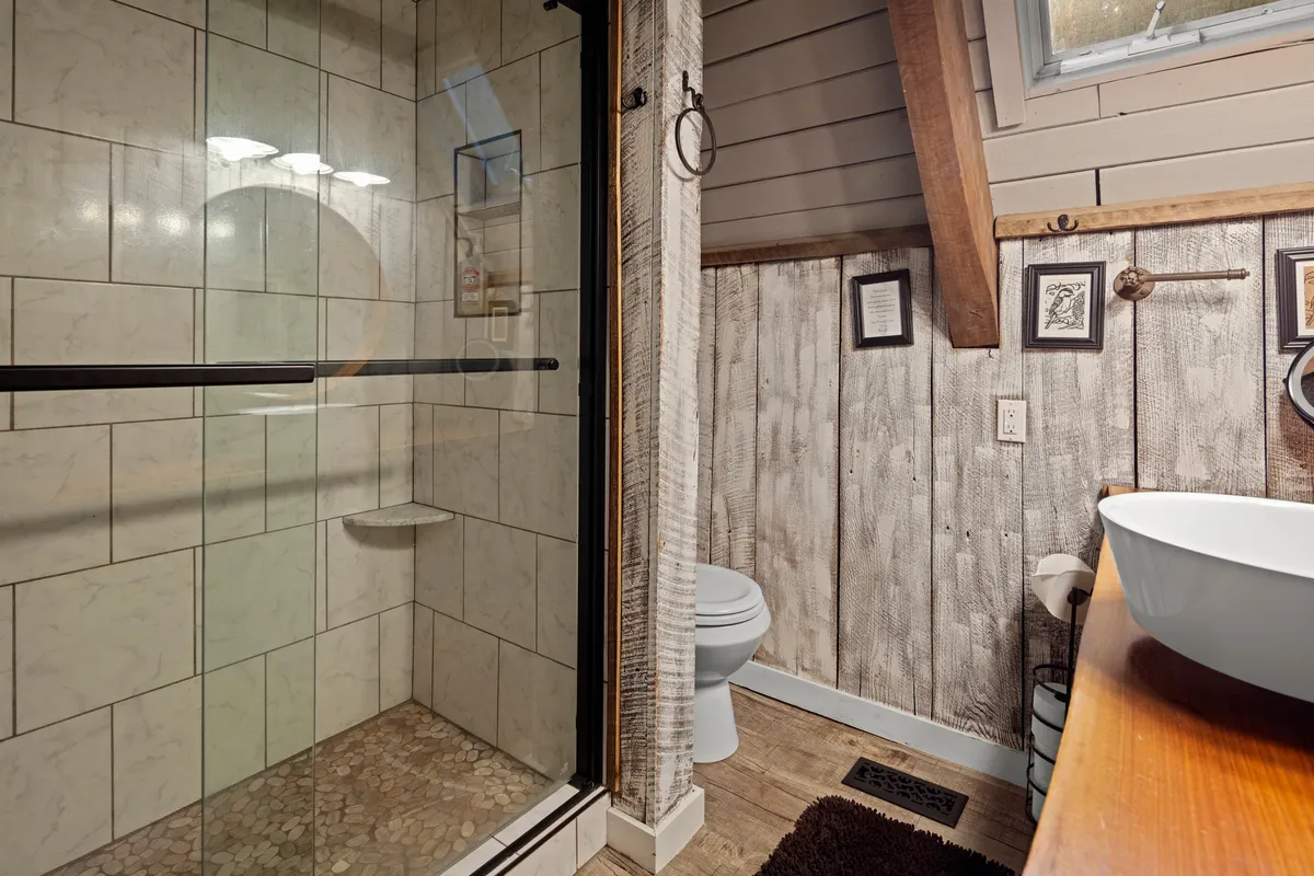 A well-appointed bathroom with a glass shower enclosure, wooden countertop, framed wall art, and textured wall. The space is warm and inviting, ideal for relaxing after outdoor adventures.