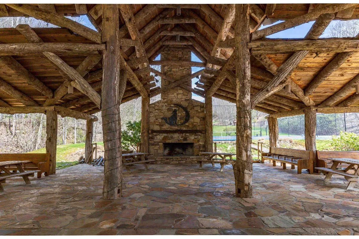 An inviting outdoor fireplace area with picnic tables and wooden beams, ideal for group gatherings and communal meals. Evening light adds warmth, suggesting the space is perfect for socializing and celebrating special occasions together.