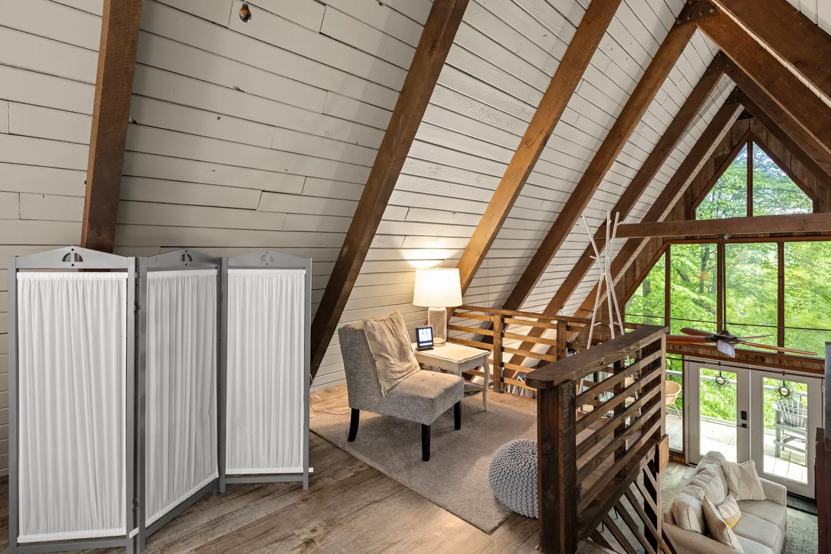 A cozy interior with exposed wooden beams, large windows, and a comfortable seating area. The space feels inviting and is positioned to take in the changing seasons, making it perfect for both winter gear stowage and summer relaxation. The visibility of nature through the windows ties the interior to year-round outdoor pursuits.