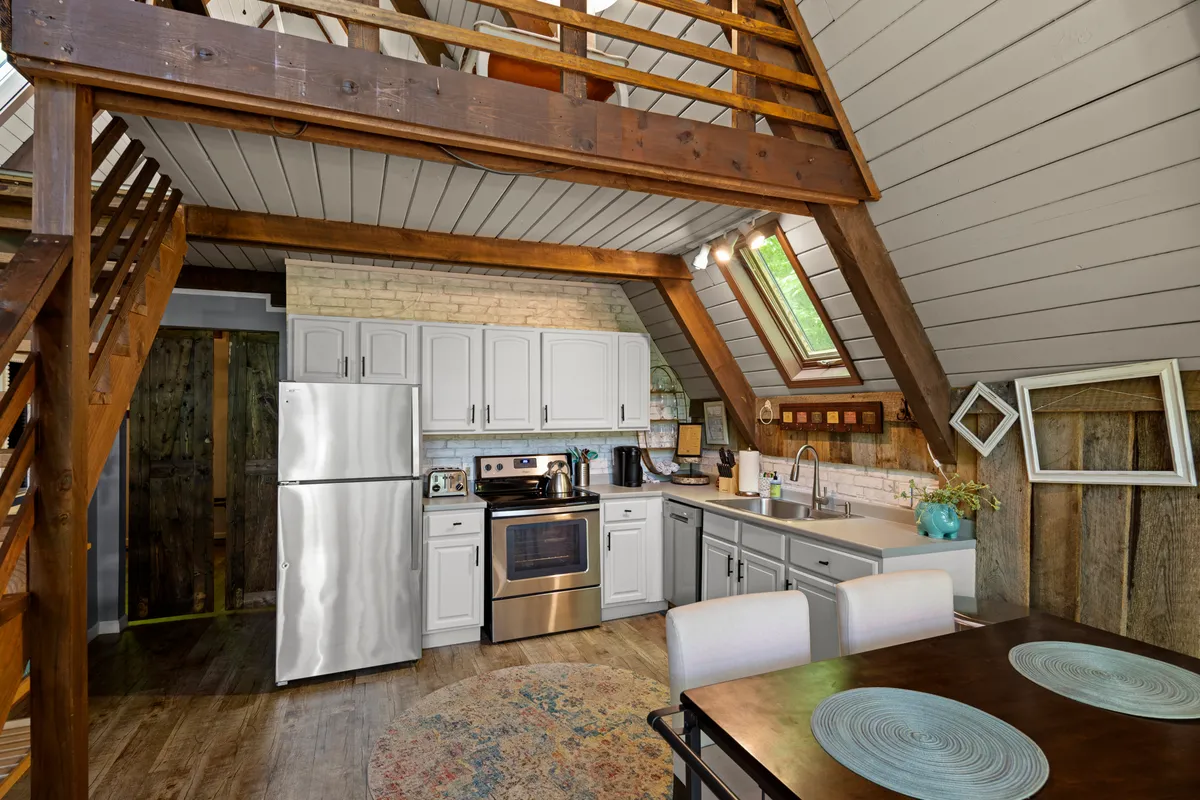 A bright and inviting kitchen-dining space features modern appliances, a generous wooden dining table, exposed beams, and large windows framing natural vistas. The design invites group cooking, shared meals, and celebrations, making it ideal for family or friendly gatherings.
